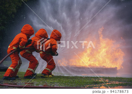 Firefighter Rescue team training in fire fighting extinguisher. Firefighter teamwork fighting with flame using fire hose chemical water foam spray engine. Fireman wear hard hat, safety suit uniform 94178673