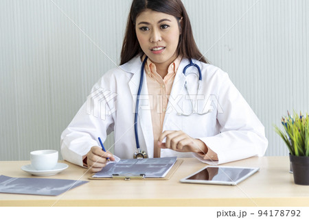 Close up hands of women doctor using laptop, tablet working medical clinic looking CAT scan xray film. women doctor write prescription medical lab hospital. Crop asian women work doctor office desk 94178792