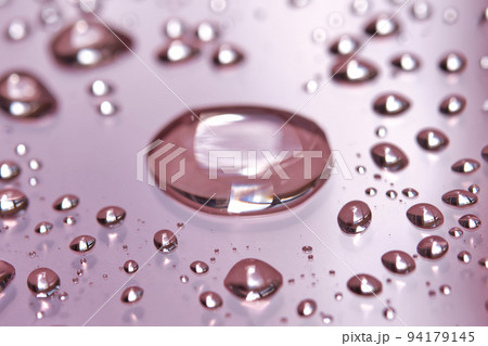 A large drop and splashes of micellar water on a pink background. 94179145
