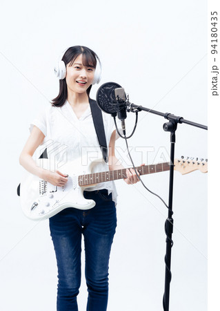 白いヘッドホンを付けて歌う若い女性、エレキギター 94180435