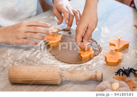 Preparing to celebrate halloween and preparing a treat. Children cut out forms of rolled ginger dough for baking halloween cookies on the table. Lifestyle Preparing to celebrate halloween and preparing a treat. Children cut out forms of rolled ginger dough for baking halloween cookies on the table. Lifestyle 94180583