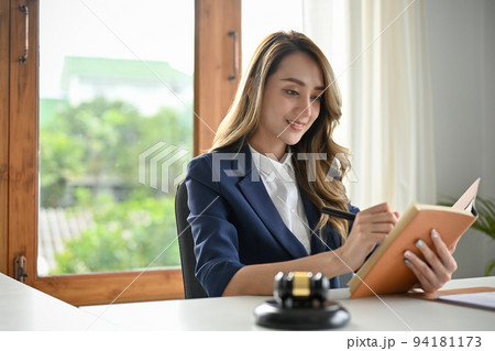 Successful Asian female lawyer reading a law book at her office desk. 94181173