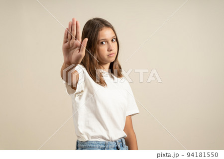 Young brunette woman in a t-shirt over isolated beige background stopping singing with her palm. Warning expression with negative and serious gesture on the face Young brunette woman in a t-shirt over isolated beige background stopping singing with her palm. Warning expression with negative and serious gesture on the face 94181550