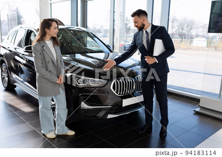 a representative of a car dealership demonstrates a car to a buyer 94183114