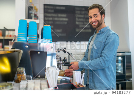 Barista making coffee in the cafe and looking contented Barista making coffee in the cafe and looking contented 94183277
