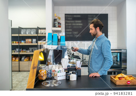 Barista making coffee in the cafe and looking contented Barista making coffee in the cafe and looking contented 94183281