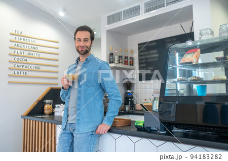 A handsome young man standing near the counter with a coffee cup A handsome young man standing near the counter with a coffee cup 94183282