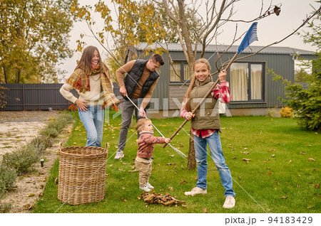 Whole family cleaning the yard with garden rakes 94183429
