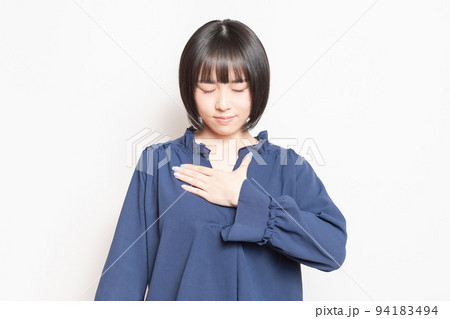 白い背景の前で、胸に手を当てる若い女性 94183494