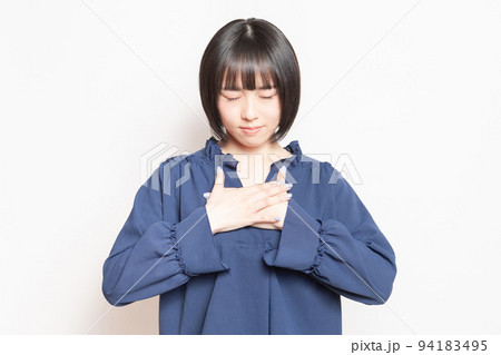 白い背景の前で、胸に手を当てる若い女性 94183495