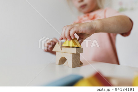 Little child girl playing wooden building blocks at home or kindergarten. Development and construction concept. Multi-colored educational bricks for early learning and education for young children. 94184191
