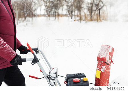 Detail of portable red snow blower powered by gasoline in action. Man outdoor using snowblower machine after snowstorm. Snow removal, thrower assistant in winter. Guy blowing snow during blizzard Detail of portable red snow blower powered by gasoline in action. Man outdoor using snowblower machine after snowstorm. Snow removal, thrower assistant in winter. Guy blowing snow during blizzard 94184192