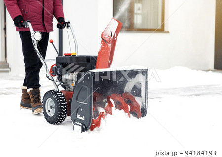 Closeup of red snow blower in action. Senior mature man outdoor in front of house using snowblower machine for removing snow on yard. Snow thrower in winter outside home. Young worker guy blowing snow Closeup of red snow blower in action. Senior mature man outdoor in front of house using snowblower machine for removing snow on yard. Snow thrower in winter outside home. Young worker guy blowing snow 94184193