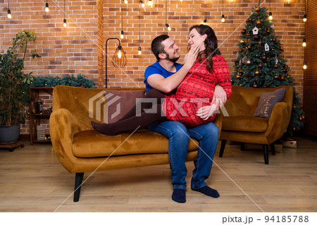 Happy future parents sit on the sofa and laugh, pregnancy and christmas. 94185788