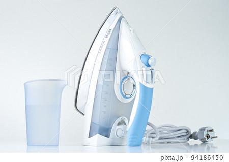 New iron with electrical cable and water for steam on white background, Modern household appliances to help with daily routine and chores New iron with electrical cable and water for steam on white background, Modern household appliances to help with daily routine and chores 94186450