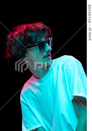 Portrait of young stylish man with mustache posing in sunglasses and white T-shirt isolated over black background in neon light 94186508