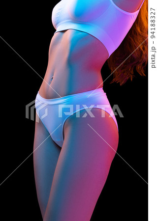 Cropped image of sportive female body in white cotton underwear isolated over dark background in neon light. Concept of beauty, fitness, health, spa Cropped image of sportive female body in white cotton underwear isolated over dark background in neon light. Concept of beauty, fitness, health, spa 94188327