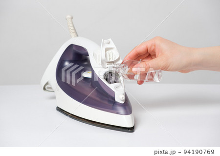 A woman pours a cleansing liquid into a water tank in an iron. Cleaning the iron from scale 94190769