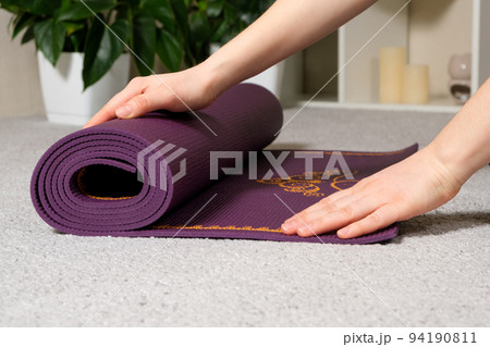A close-up of a woman's hands roll out a purple mat for yoga or fitness at home 94190811