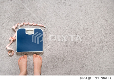 Bare feet and a floor blue scale with a measuring centimeter tape, the concept of losing weight, place for text, top view. 94190813