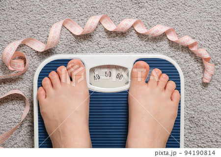 Women's bare feet on floor scales and the number 51 kilograms on the scale, a centimeter tape. The idea of losing weight and controlling weight 94190814