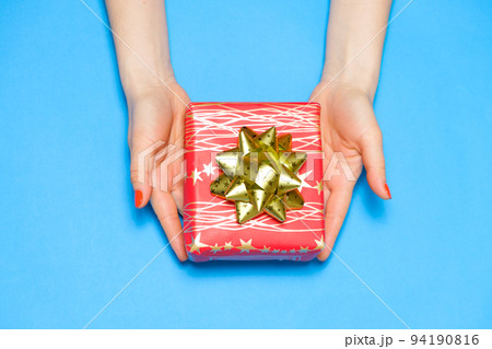Beautiful red gift box with bow in women's hands, top view, copy space for text. 94190816