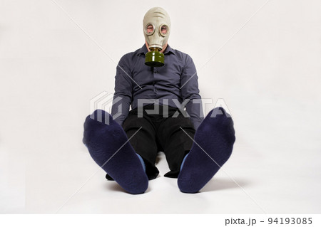 A man in a gas mask sits on a white background, his legs stinking. Unpleasant smell of socks in men. A man in a gas mask sits on a white background, his legs stinking. Unpleasant smell of socks in men. 94193085