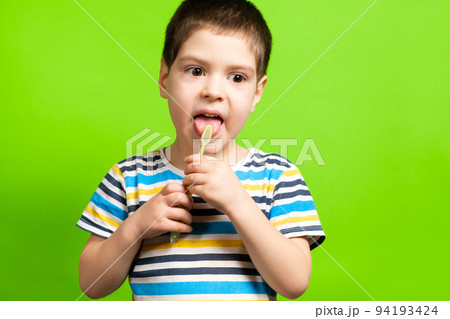 A preschool boy of 4 years cleans with a toothbrush a tongue on a green background. 94193424