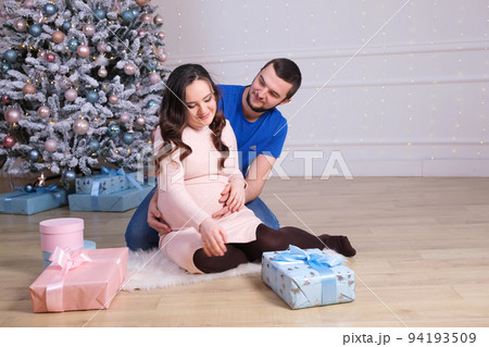A happy husband and wife are preparing to become parents, having fun near the Christmas tree. Pregnancy and Christmas 94193509