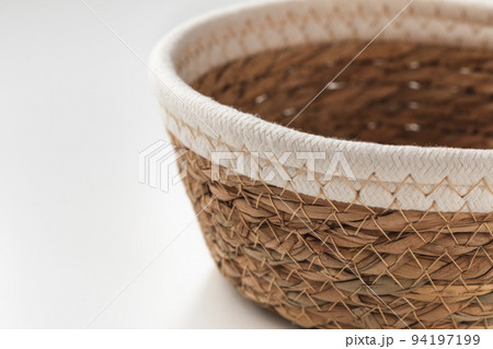 Small round seagrass and cream white cotton rope storage basket with rim. Trendy natural multifunctional table container for fruits and hobbies. Close-up, copy space 94197199