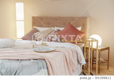 Bedroom interior in light colors with wooden furniture and pillows. Lamps on both sides. 94199811