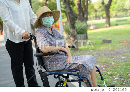 Help Asian senior or elderly old lady woman on wheelchair and wearing a face mask for protect safety infection Covid19 Coronavirus in park. 94201166