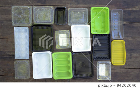 Multi-colored disposable plastic food containers are laid out on a wooden floor. plastic pollution 94202040
