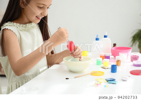 Cute little girl mixing ingredients with silicone spatula at table in room. DIY slime toy Cute little girl mixing ingredients with silicone spatula at table in room. DIY slime toy 94202733