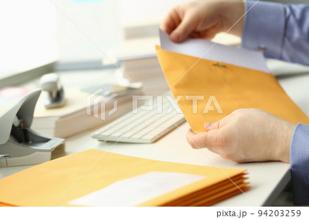 Businessman takes out documents from yellow envelope Businessman takes out documents from yellow envelope 94203259