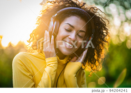 Close-up of african american woman listening to music with headphones outdoors. Young girl with 94204241