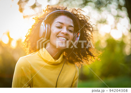 Close-up of african american woman listening to music with headphones outdoors. Young girl with Close-up of african american woman listening to music with headphones outdoors. Young girl with 94204308