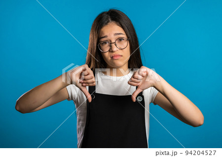 Young asian girl standing on blue studio background expressing discontent and showing thumb down Young asian girl standing on blue studio background expressing discontent and showing thumb down 94204527