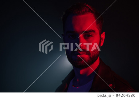 Portrait of young caucasian man with beard in leather jacket illuminated neon light looking at 94204530