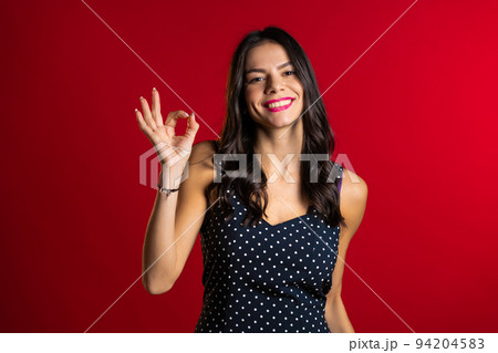 Young woman with perfect make-up making OK sign over red background. Winner. Success. Positive girl 94204583