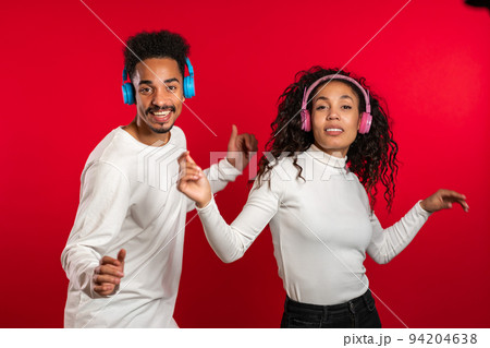 Young african american couple dancing with headphones isolated on red background studio. Party Young african american couple dancing with headphones isolated on red background studio. Party 94204638