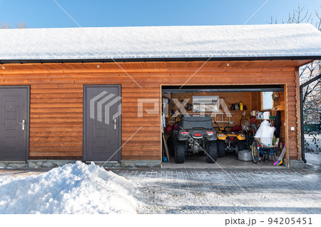 Facade view open door ATV home garage with quad bikes offroad vehicle parked sunny snowy cold winter day. ATV adventure extreme sport. House organized clutter warehouse tools equipment shed storage Facade view open door ATV home garage with quad bikes offroad vehicle parked sunny snowy cold winter day. ATV adventure extreme sport. House organized clutter warehouse tools equipment shed storage 94205451