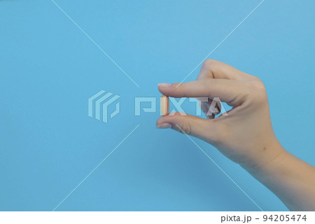 A woman holds a headache pill in her hand on a blue background, vitamins or medicine. Treatment from virus, disease. Health care, medicine. 94205474