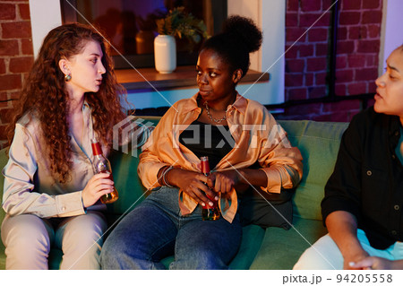 Three young intercultural women with bottles of beer relaxing on couch 94205558