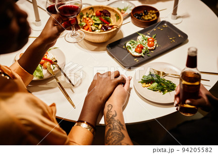 Hands of two young lesbian women with alcoholic drinks sitting by served table 94205582
