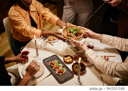 Above angle of hands of young man passing wooden bowl with salad to friend Above angle of hands of young man passing wooden bowl with salad to friend 94205586