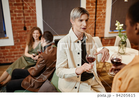 Young gay man in white casualwear holding glass of red wine and talking to girl 94205615
