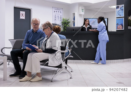 Diverse medical team working at reception desk, filling in checkup report papers and making appointments. Nurse and receptionist doing registration work in hospital waiting room. Diverse medical team working at reception desk, filling in checkup report papers and making appointments. Nurse and receptionist doing registration work in hospital waiting room. 94207482