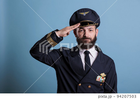 Confident airplane pilot saluting, wearing uniform and hat front view portrait, plane captain looking at camera. Civil aviator with airline wings badge on jacket, professional aircrew member Confident airplane pilot saluting, wearing uniform and hat front view portrait, plane captain looking at camera. Civil aviator with airline wings badge on jacket, professional aircrew member 94207503