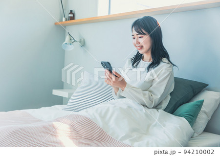 ベットでスマホをみる女性 94210002